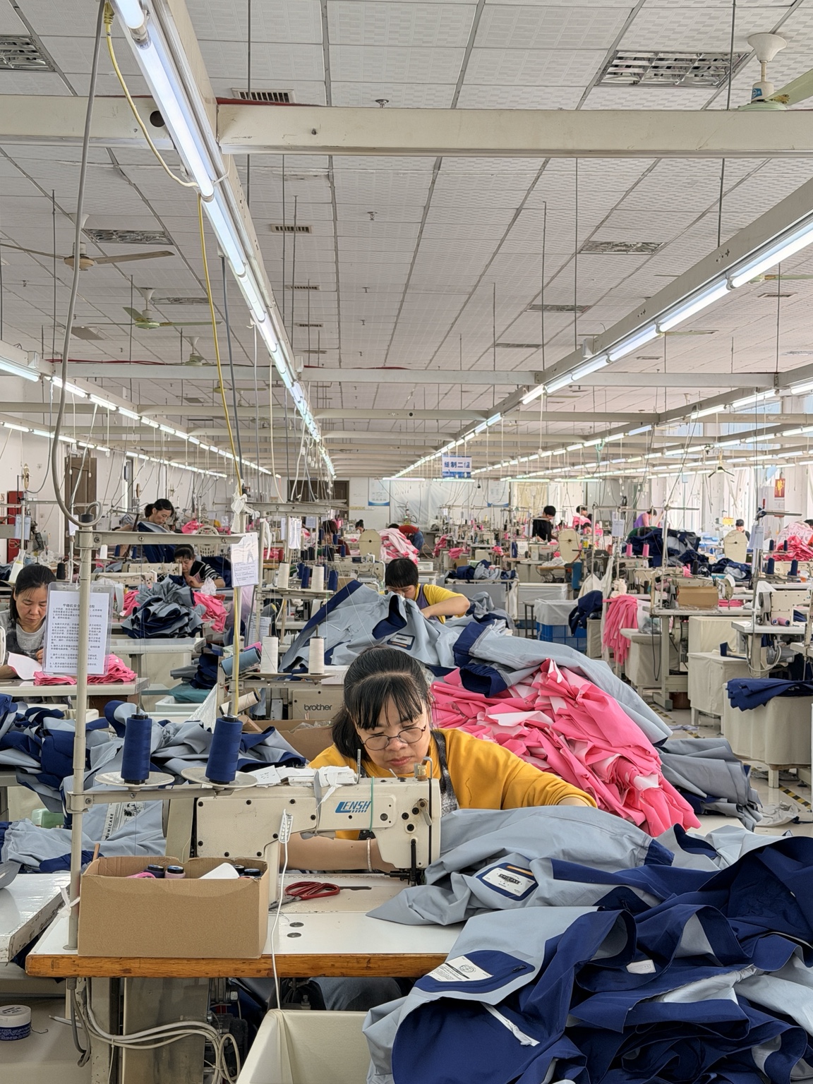 森纺工厂实拍：师傅在缝纫机前制作服装，周围摆放裁片与在制品